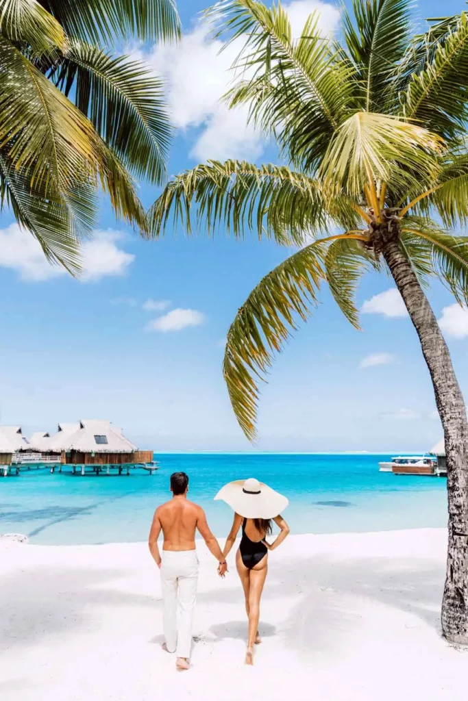 a couple on a beach with overwater bungalows on the background
