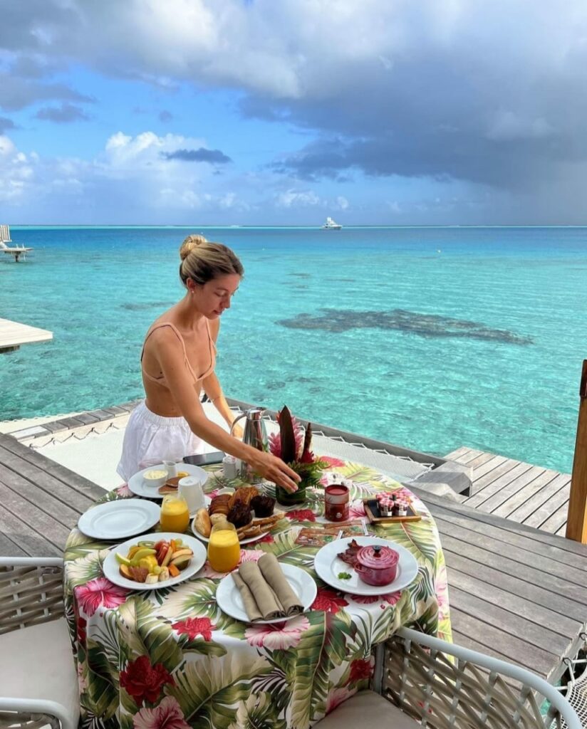 a woman having a breakfast on an Overwater bungalow deck at the Conrad Bora Bora Nui