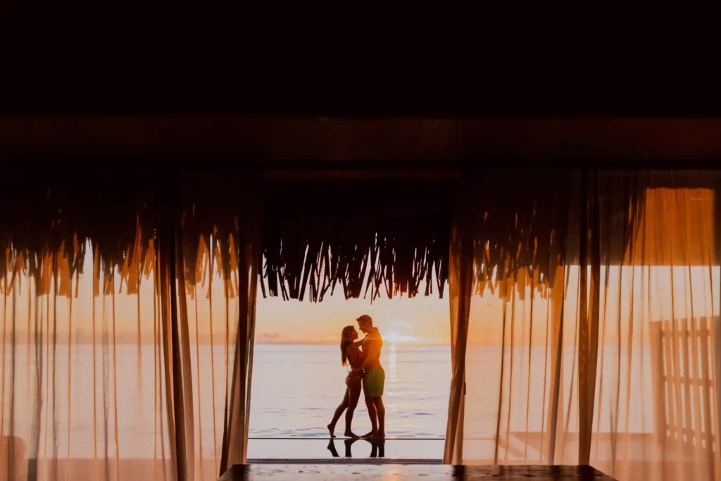 a couple standing on an Overwater bungalow with the sunset