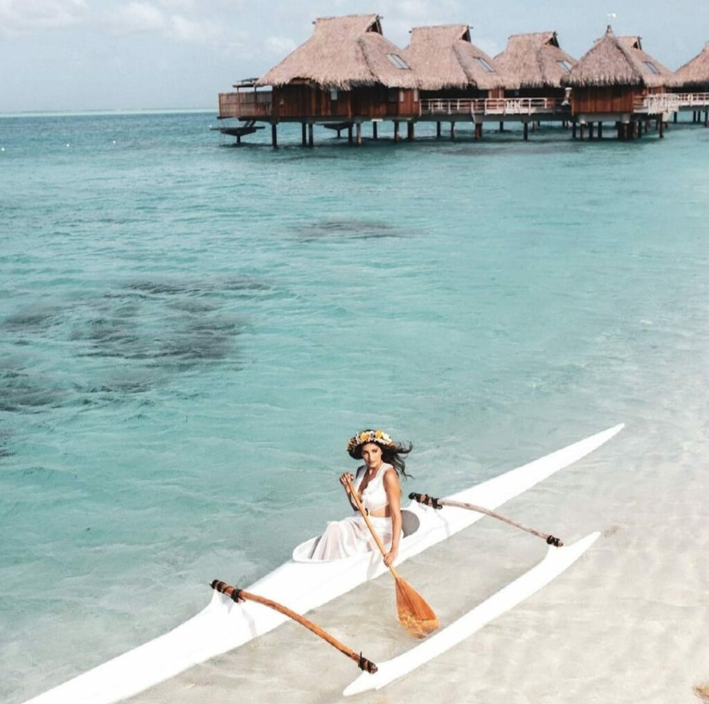 a woman in a traditional canoe with overwater bungalows on the background