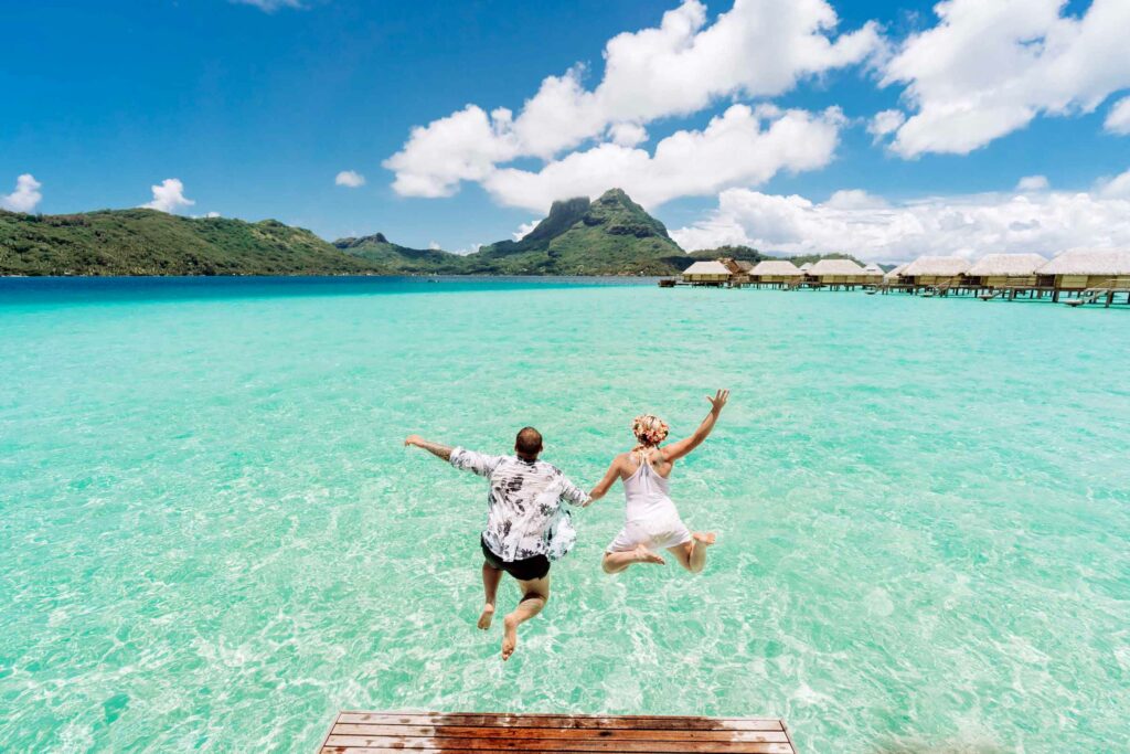 A couple jumping off an overwater bungalow